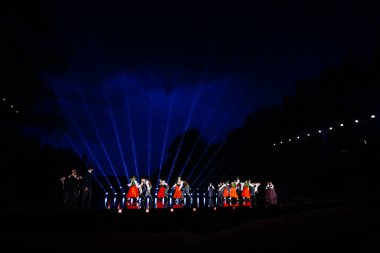 Valmiera, Letonya - 7 Haziran 2025 - GAUJA 80 'deki geleneksel Letonya halk dansları kolajı, renkli kostümlü dansçıları gece aydınlatmalı bir sahnede sergiliyorlar..