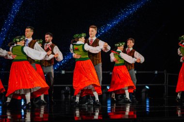 Valmiera, Letonya - 7 Haziran 2025 - GAUJA 80 'deki geleneksel Letonya halk dansları kolajı, renkli kostümlü dansçıları gece aydınlatmalı bir sahnede sergiliyorlar..