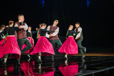 Valmiera, Letonya - 7 Haziran 2025 - GAUJA 80 'deki geleneksel Letonya halk dansları kolajı, renkli kostümlü dansçıları gece aydınlatmalı bir sahnede sergiliyorlar..