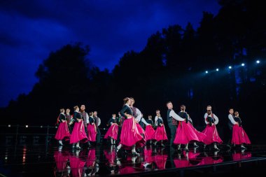 Valmiera, Letonya - 7 Haziran 2025 - GAUJA 80 'deki geleneksel Letonya halk dansları kolajı, renkli kostümlü dansçıları gece aydınlatmalı bir sahnede sergiliyorlar..