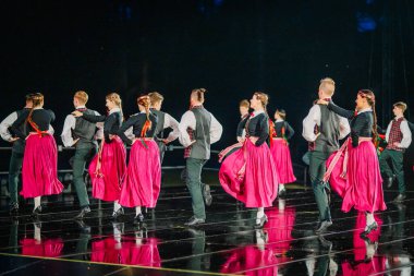 Valmiera, Letonya - 7 Haziran 2025 - GAUJA 80 'deki geleneksel Letonya halk dansları kolajı, renkli kostümlü dansçıları gece aydınlatmalı bir sahnede sergiliyorlar..