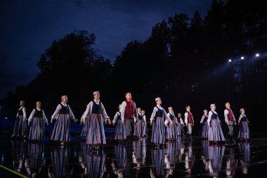 Valmiera, Letonya - 7 Haziran 2025 - GAUJA 80 'deki geleneksel Letonya halk dansları kolajı, renkli kostümlü dansçıları gece aydınlatmalı bir sahnede sergiliyorlar..