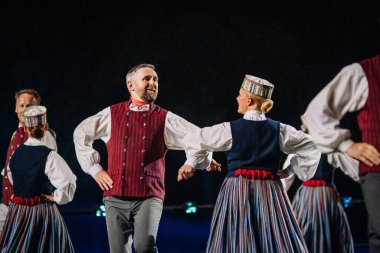 Valmiera, Letonya - 7 Haziran 2025 - GAUJA 80 'deki geleneksel Letonya halk dansları kolajı, renkli kostümlü dansçıları gece aydınlatmalı bir sahnede sergiliyorlar..