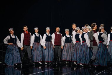 Valmiera, Letonya - 7 Haziran 2025 - GAUJA 80 'deki geleneksel Letonya halk dansları kolajı, renkli kostümlü dansçıları gece aydınlatmalı bir sahnede sergiliyorlar..