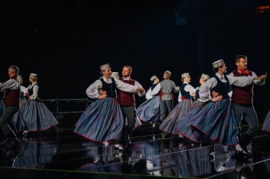 Valmiera, Letonya - 7 Haziran 2025 - GAUJA 80 'deki geleneksel Letonya halk dansları kolajı, renkli kostümlü dansçıları gece aydınlatmalı bir sahnede sergiliyorlar..