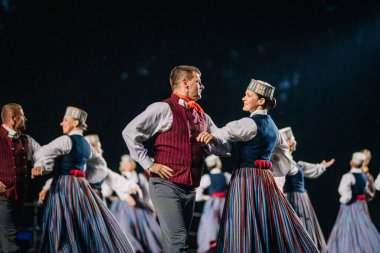 Valmiera, Letonya - 7 Haziran 2025 - GAUJA 80 'deki geleneksel Letonya halk dansları kolajı, renkli kostümlü dansçıları gece aydınlatmalı bir sahnede sergiliyorlar..