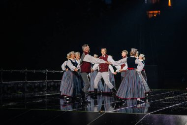 Valmiera, Letonya - 7 Haziran 2025 - GAUJA 80 'deki geleneksel Letonya halk dansları kolajı, renkli kostümlü dansçıları gece aydınlatmalı bir sahnede sergiliyorlar..