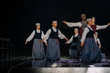 Valmiera, Letonya - 7 Haziran 2025 - GAUJA 80 'deki geleneksel Letonya halk dansları kolajı, renkli kostümlü dansçıları gece aydınlatmalı bir sahnede sergiliyorlar..