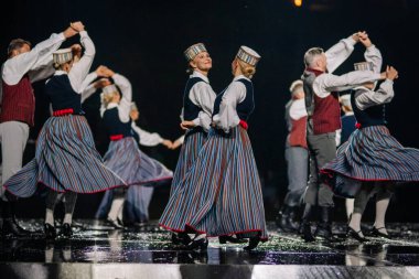 Valmiera, Letonya - 7 Haziran 2025 - GAUJA 80 'deki geleneksel Letonya halk dansları kolajı, renkli kostümlü dansçıları gece aydınlatmalı bir sahnede sergiliyorlar..