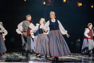 Valmiera, Letonya - 7 Haziran 2025 - GAUJA 80 'deki geleneksel Letonya halk dansları kolajı, renkli kostümlü dansçıları gece aydınlatmalı bir sahnede sergiliyorlar..