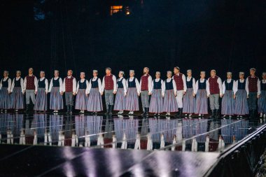 Valmiera, Letonya - 7 Haziran 2025 - GAUJA 80 'deki geleneksel Letonya halk dansları kolajı, renkli kostümlü dansçıları gece aydınlatmalı bir sahnede sergiliyorlar..