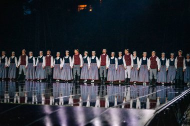 Valmiera, Letonya - 7 Haziran 2025 - GAUJA 80 'deki geleneksel Letonya halk dansları kolajı, renkli kostümlü dansçıları gece aydınlatmalı bir sahnede sergiliyorlar..