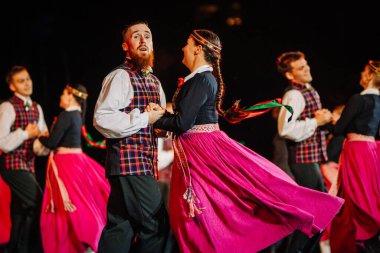 Valmiera, Letonya - 7 Haziran 2025 - GAUJA 80 'deki geleneksel Letonya halk dansları kolajı, renkli kostümlü dansçıları gece aydınlatmalı bir sahnede sergiliyorlar..