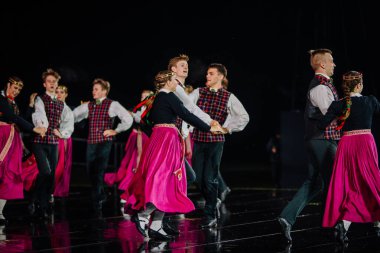 Valmiera, Letonya - 7 Haziran 2025 - GAUJA 80 'deki geleneksel Letonya halk dansları kolajı, renkli kostümlü dansçıları gece aydınlatmalı bir sahnede sergiliyorlar..