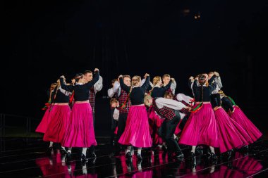 Valmiera, Letonya - 7 Haziran 2025 - GAUJA 80 'deki geleneksel Letonya halk dansları kolajı, renkli kostümlü dansçıları gece aydınlatmalı bir sahnede sergiliyorlar..