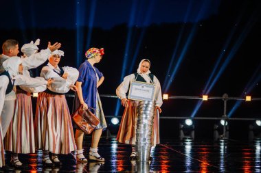 Valmiera, Letonya - 7 Haziran 2025 - GAUJA 80 'deki geleneksel Letonya halk dansları kolajı, renkli kostümlü dansçıları gece aydınlatmalı bir sahnede sergiliyorlar..