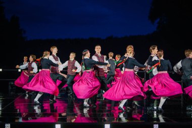 Valmiera, Letonya - 7 Haziran 2025 - GAUJA 80 'deki geleneksel Letonya halk dansları kolajı, renkli kostümlü dansçıları gece aydınlatmalı bir sahnede sergiliyorlar..