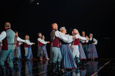 Valmiera, Letonya - 7 Haziran 2025 - GAUJA 80 'deki geleneksel Letonya halk dansları kolajı, renkli kostümlü dansçıları gece aydınlatmalı bir sahnede sergiliyorlar..