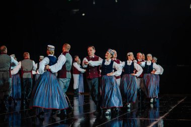 Valmiera, Letonya - 7 Haziran 2025 - GAUJA 80 'deki geleneksel Letonya halk dansları kolajı, renkli kostümlü dansçıları gece aydınlatmalı bir sahnede sergiliyorlar..