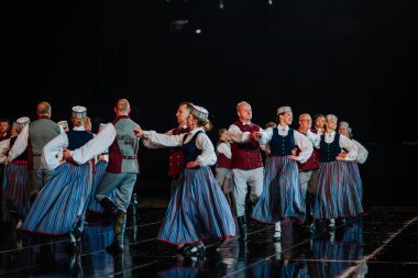 Valmiera, Letonya - 7 Haziran 2025 - GAUJA 80 'deki geleneksel Letonya halk dansları kolajı, renkli kostümlü dansçıları gece aydınlatmalı bir sahnede sergiliyorlar..