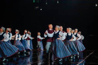 Valmiera, Letonya - 7 Haziran 2025 - GAUJA 80 'deki geleneksel Letonya halk dansları kolajı, renkli kostümlü dansçıları gece aydınlatmalı bir sahnede sergiliyorlar..