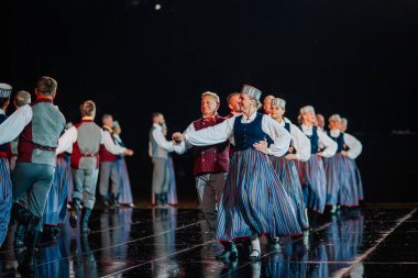 Valmiera, Letonya - 7 Haziran 2025 - GAUJA 80 'deki geleneksel Letonya halk dansları kolajı, renkli kostümlü dansçıları gece aydınlatmalı bir sahnede sergiliyorlar..