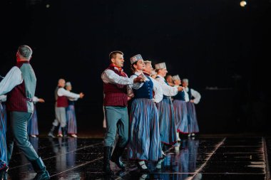 Valmiera, Letonya - 7 Haziran 2025 - GAUJA 80 'deki geleneksel Letonya halk dansları kolajı, renkli kostümlü dansçıları gece aydınlatmalı bir sahnede sergiliyorlar..