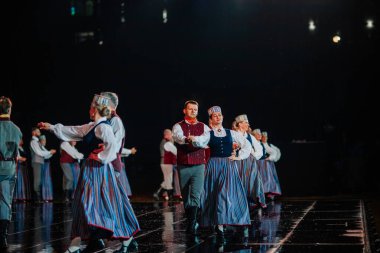 Valmiera, Letonya - 7 Haziran 2025 - GAUJA 80 'deki geleneksel Letonya halk dansları kolajı, renkli kostümlü dansçıları gece aydınlatmalı bir sahnede sergiliyorlar..