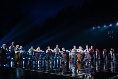 Valmiera, Letonya - 7 Haziran 2025 - GAUJA 80 'deki geleneksel Letonya halk dansları kolajı, renkli kostümlü dansçıları gece aydınlatmalı bir sahnede sergiliyorlar..