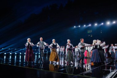 Valmiera, Letonya - 7 Haziran 2025 - GAUJA 80 'deki geleneksel Letonya halk dansları kolajı, renkli kostümlü dansçıları gece aydınlatmalı bir sahnede sergiliyorlar..