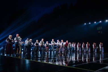 Valmiera, Letonya - 7 Haziran 2025 - GAUJA 80 'deki geleneksel Letonya halk dansları kolajı, renkli kostümlü dansçıları gece aydınlatmalı bir sahnede sergiliyorlar..