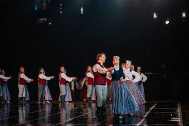 Valmiera, Letonya - 7 Haziran 2025 - GAUJA 80 'deki geleneksel Letonya halk dansları kolajı, renkli kostümlü dansçıları gece aydınlatmalı bir sahnede sergiliyorlar..