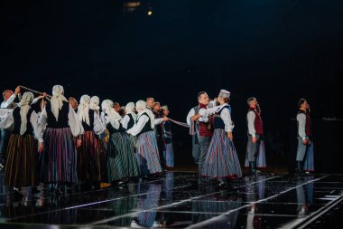 Valmiera, Letonya - 7 Haziran 2025 - GAUJA 80 'deki geleneksel Letonya halk dansları kolajı, renkli kostümlü dansçıları gece aydınlatmalı bir sahnede sergiliyorlar..