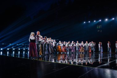 Valmiera, Letonya - 7 Haziran 2025 - GAUJA 80 'deki geleneksel Letonya halk dansları kolajı, renkli kostümlü dansçıları gece aydınlatmalı bir sahnede sergiliyorlar..