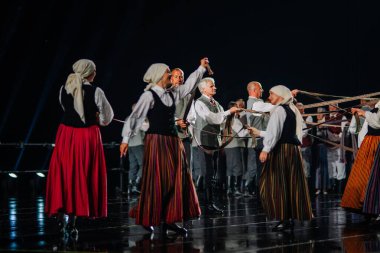 Valmiera, Letonya - 7 Haziran 2025 - GAUJA 80 'deki geleneksel Letonya halk dansları kolajı, renkli kostümlü dansçıları gece aydınlatmalı bir sahnede sergiliyorlar..