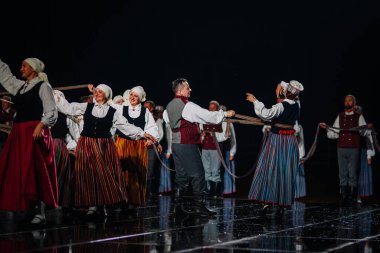 Valmiera, Letonya - 7 Haziran 2025 - GAUJA 80 'deki geleneksel Letonya halk dansları kolajı, renkli kostümlü dansçıları gece aydınlatmalı bir sahnede sergiliyorlar..
