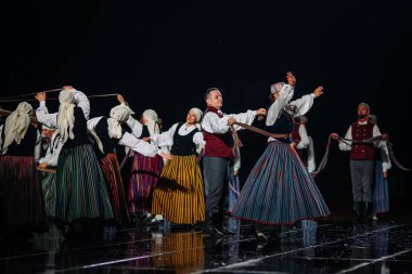 Valmiera, Letonya - 7 Haziran 2025 - GAUJA 80 'deki geleneksel Letonya halk dansları kolajı, renkli kostümlü dansçıları gece aydınlatmalı bir sahnede sergiliyorlar..