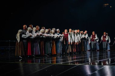 Valmiera, Letonya - 7 Haziran 2025 - GAUJA 80 'deki geleneksel Letonya halk dansları kolajı, renkli kostümlü dansçıları gece aydınlatmalı bir sahnede sergiliyorlar..
