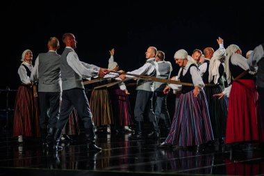 Valmiera, Letonya - 7 Haziran 2025 - GAUJA 80 'deki geleneksel Letonya halk dansları kolajı, renkli kostümlü dansçıları gece aydınlatmalı bir sahnede sergiliyorlar..