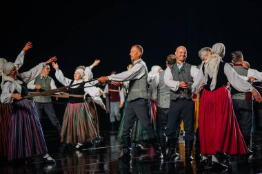 Valmiera, Letonya - 7 Haziran 2025 - GAUJA 80 'deki geleneksel Letonya halk dansları kolajı, renkli kostümlü dansçıları gece aydınlatmalı bir sahnede sergiliyorlar..