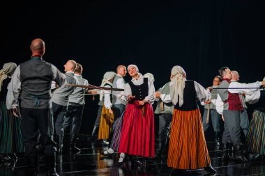 Valmiera, Letonya - 7 Haziran 2025 - GAUJA 80 'deki geleneksel Letonya halk dansları kolajı, renkli kostümlü dansçıları gece aydınlatmalı bir sahnede sergiliyorlar..