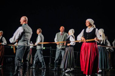 Valmiera, Letonya - 7 Haziran 2025 - GAUJA 80 'deki geleneksel Letonya halk dansları kolajı, renkli kostümlü dansçıları gece aydınlatmalı bir sahnede sergiliyorlar..