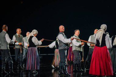 Valmiera, Letonya - 7 Haziran 2025 - GAUJA 80 'deki geleneksel Letonya halk dansları kolajı, renkli kostümlü dansçıları gece aydınlatmalı bir sahnede sergiliyorlar..