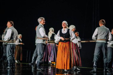 Valmiera, Letonya - 7 Haziran 2025 - GAUJA 80 'deki geleneksel Letonya halk dansları kolajı, renkli kostümlü dansçıları gece aydınlatmalı bir sahnede sergiliyorlar..