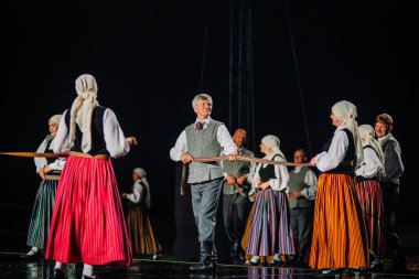 Valmiera, Letonya - 7 Haziran 2025 - GAUJA 80 'deki geleneksel Letonya halk dansları kolajı, renkli kostümlü dansçıları gece aydınlatmalı bir sahnede sergiliyorlar..