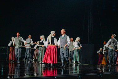 Valmiera, Letonya - 7 Haziran 2025 - GAUJA 80 'deki geleneksel Letonya halk dansları kolajı, renkli kostümlü dansçıları gece aydınlatmalı bir sahnede sergiliyorlar..
