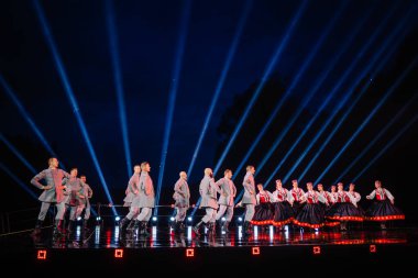 Valmiera, Letonya - 7 Haziran 2025 - GAUJA 80 'deki geleneksel Letonya halk dansları kolajı, renkli kostümlü dansçıları gece aydınlatmalı bir sahnede sergiliyorlar..