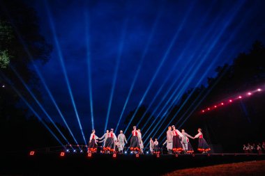 Valmiera, Letonya - 7 Haziran 2025 - GAUJA 80 'deki geleneksel Letonya halk dansları kolajı, renkli kostümlü dansçıları gece aydınlatmalı bir sahnede sergiliyorlar..