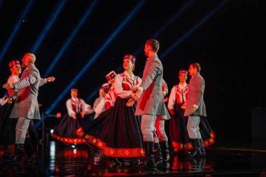 Valmiera, Letonya - 7 Haziran 2025 - GAUJA 80 'deki geleneksel Letonya halk dansları kolajı, renkli kostümlü dansçıları gece aydınlatmalı bir sahnede sergiliyorlar..