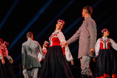 Valmiera, Letonya - 7 Haziran 2025 - GAUJA 80 'deki geleneksel Letonya halk dansları kolajı, renkli kostümlü dansçıları gece aydınlatmalı bir sahnede sergiliyorlar..